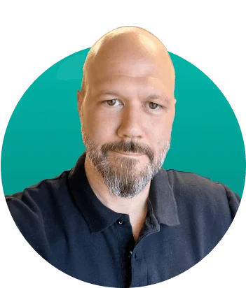 Adult man with shaved head and trimmed gray beard looks directly at the camera, wearing a dark polo; isolated in front of a teal circular gradient...