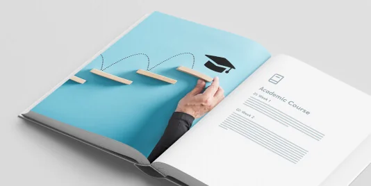 Open booklet shows a hand placing wooden step pieces forming a dotted path toward a mortarboard; pages rest on a light surface.