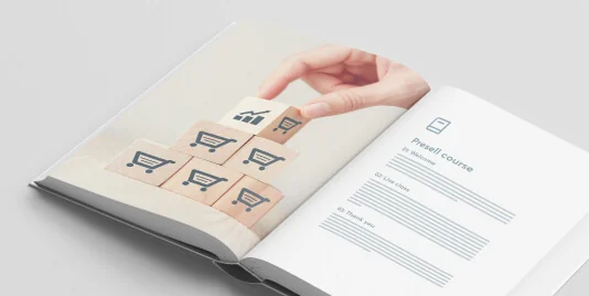 Open book showing a hand placing the top wooden cube onto a pyramid of cubes printed with shopping-cart icons; right page shows a course layout...