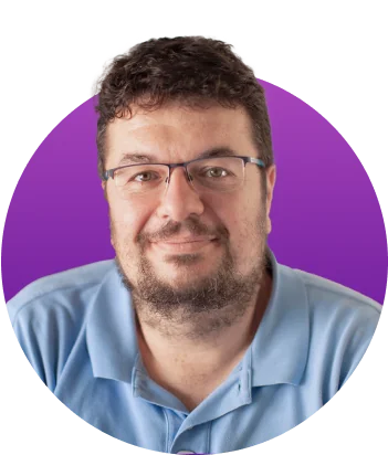 Bearded man wearing glasses and a light blue polo smiles slightly, facing the camera in a head-and-shoulders portrait against a purple circular...