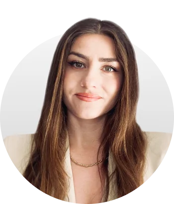 Woman with long brown hair gazes at the camera, smiling slightly; wearing a beige blazer and delicate gold chain, set against a soft circular...