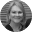 Portrait of a smiling woman, looking toward camera, wearing a blazer and pendant necklace; photograph cropped to a circular grayscale headshot with...