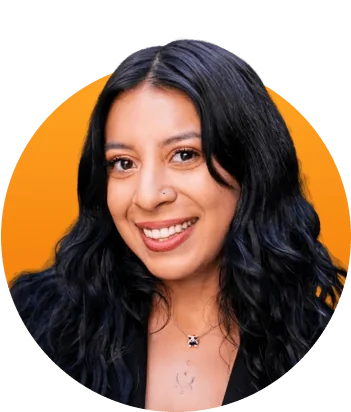 Woman with long dark wavy hair smiling directly at the camera, wearing a small pendant necklace and black top, centered against a bright orange...