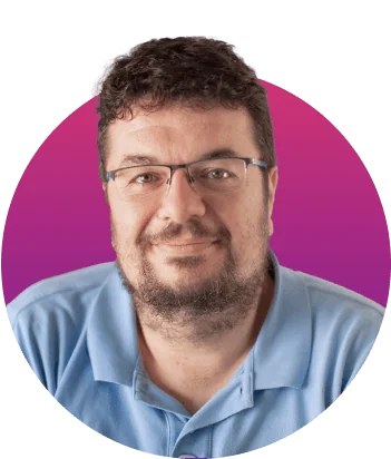Man portrait looks toward camera, smiling slightly; wearing glasses and a light blue polo, with short curly dark hair and trimmed beard, set against...