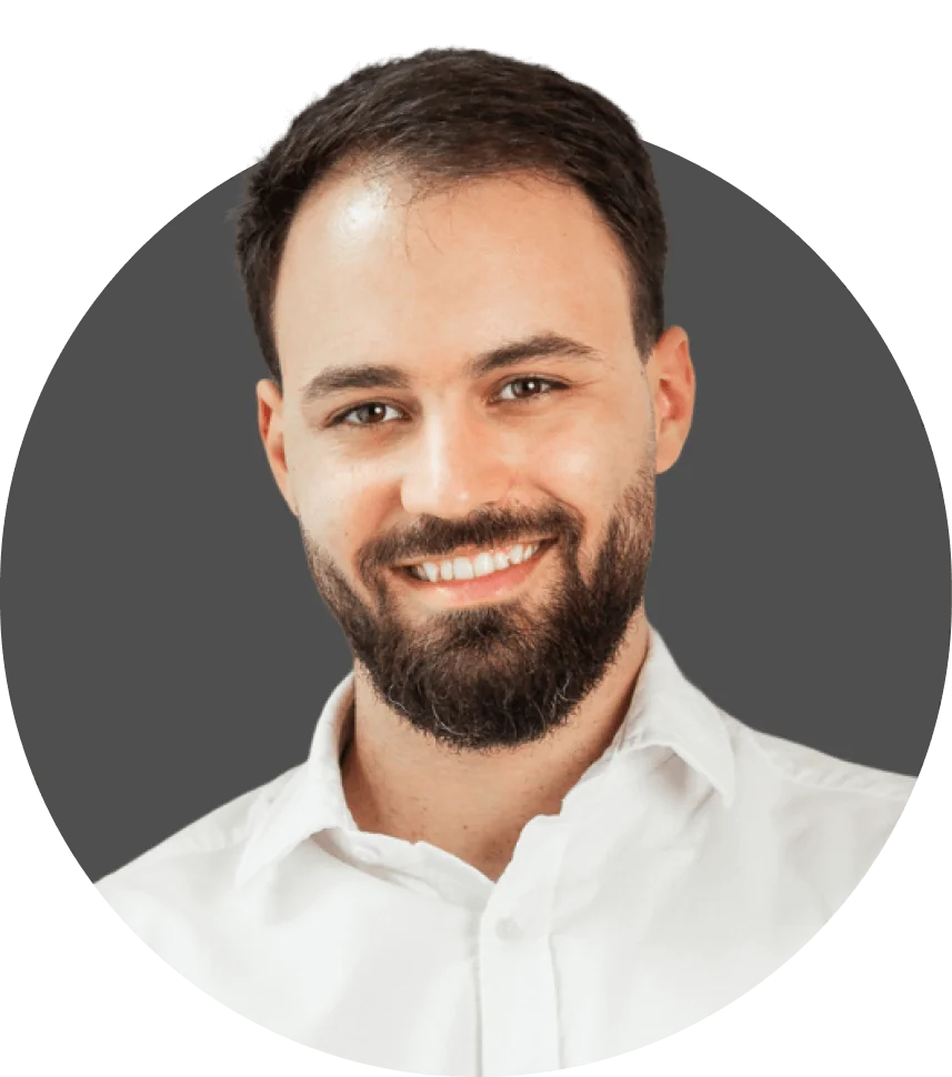 Bearded man smiling and looking at the camera, wearing a white collared shirt against a neutral gray circular backdrop; head-and-shoulders portrait...