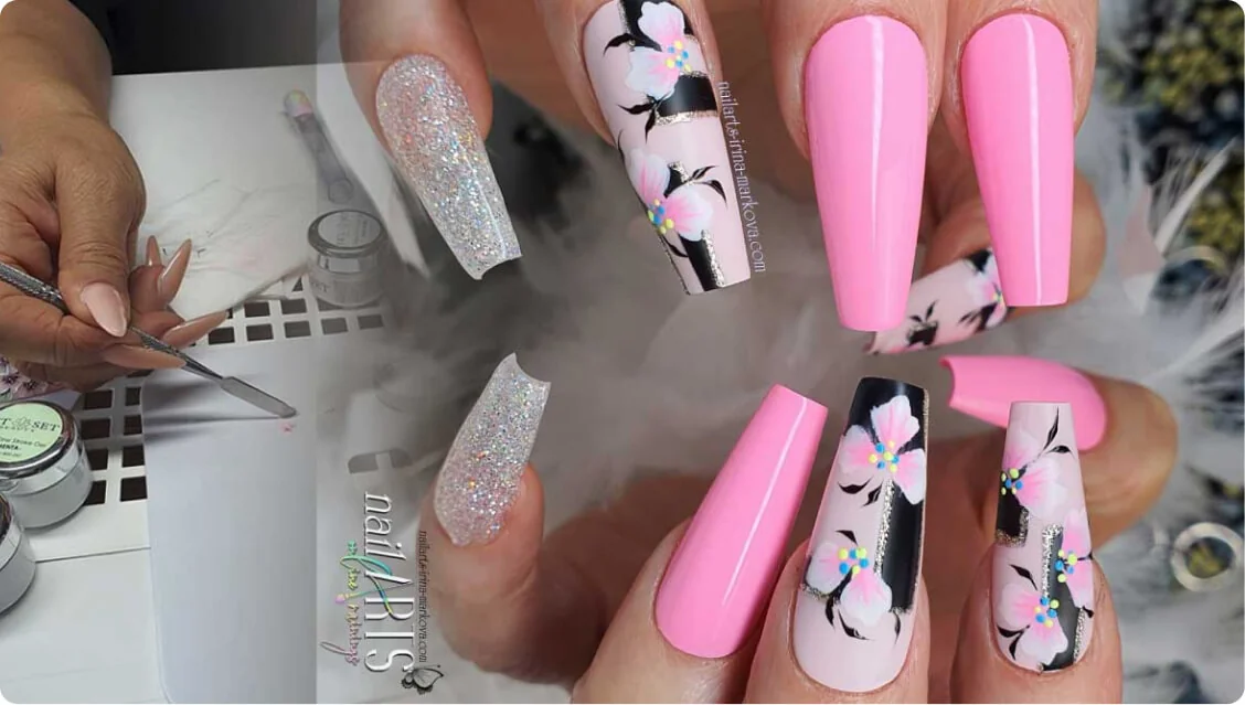 Coffin-shaped acrylic nails fanned, showing glossy pink, holographic glitter, and black-accented floral designs; held above a manicure workstation...