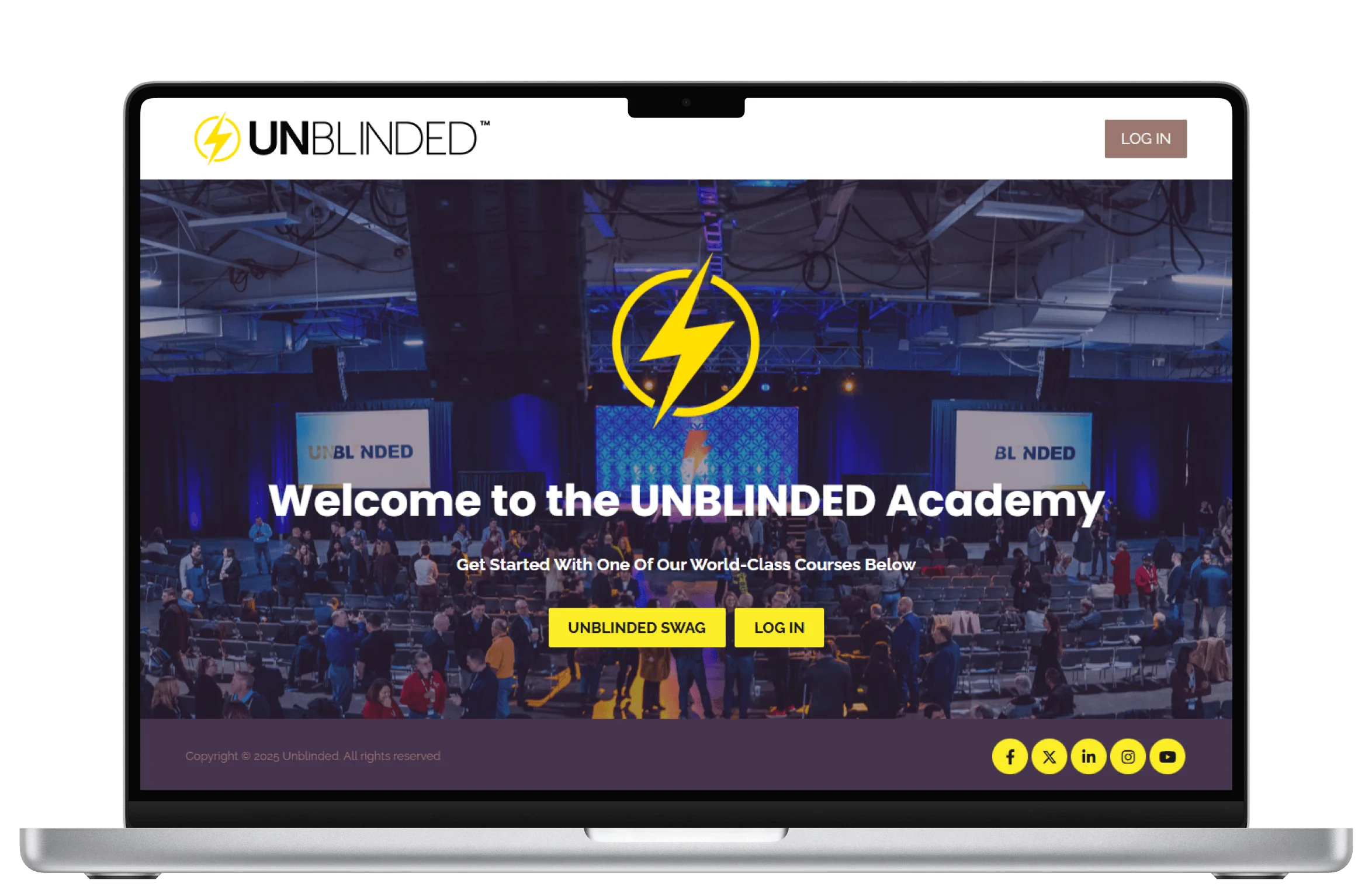 Laptop screen shows the UNBLINDED Academy homepage: a large yellow lightning logo above a conference crowd, bold welcome headline, and two yellow...