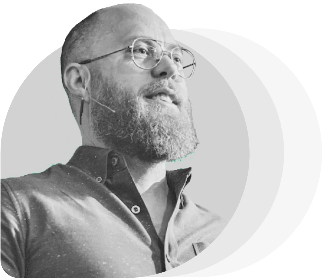 Bearded man wearing round glasses speaks into a headset microphone, looking upward.