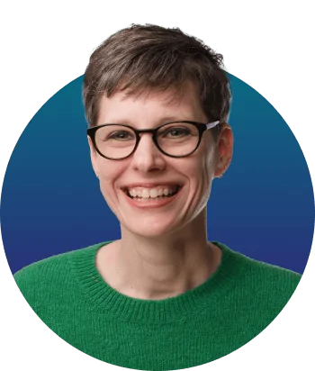 Person with short hair and black-rim glasses smiles broadly at camera, wearing a green sweater against a circular blue-to-teal gradient background.