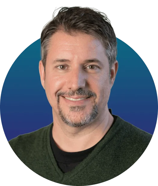 Adult man, head-and-shoulders, smiling at camera; short graying hair and trimmed goatee; wearing green V-neck sweater over black shirt; circular...