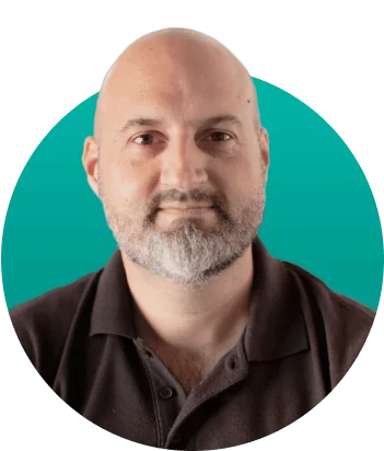 Bald man with trimmed gray beard gazes directly at the camera, wearing a dark polo; centered portrait set against a teal circular backdrop with soft,...
