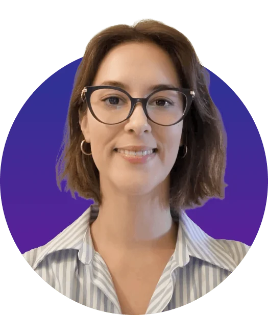 Person with short brown hair wearing cat-eye glasses and hoop earrings smiles at the camera, wearing a striped collared shirt against a circular...