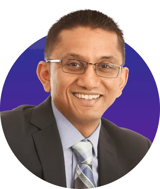 A smiling man wearing glasses and a dark suit leans slightly forward; light-blue shirt and patterned tie visible, centered in a circular crop over a...