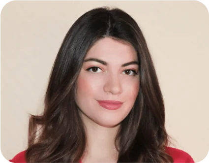 Young woman with long dark brown hair smiles subtly, facing the camera; she wears a red top against a plain beige background.