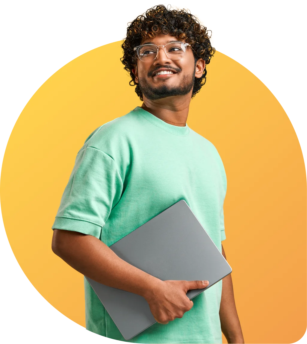 Person with curly hair and glasses holds a closed laptop against their torso, smiling and looking upward; wearing a mint-green shirt in front of a...