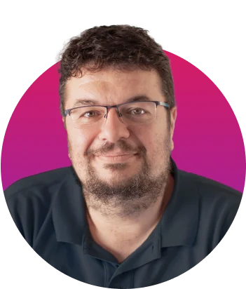 Man with glasses and short curly dark hair smiles softly while facing the camera; wearing a dark polo and trimmed beard; magenta circular backdrop...