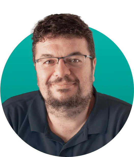 Man with glasses smiles gently, facing camera; wearing a dark polo with short curly hair and trimmed beard; teal circular background frames a...