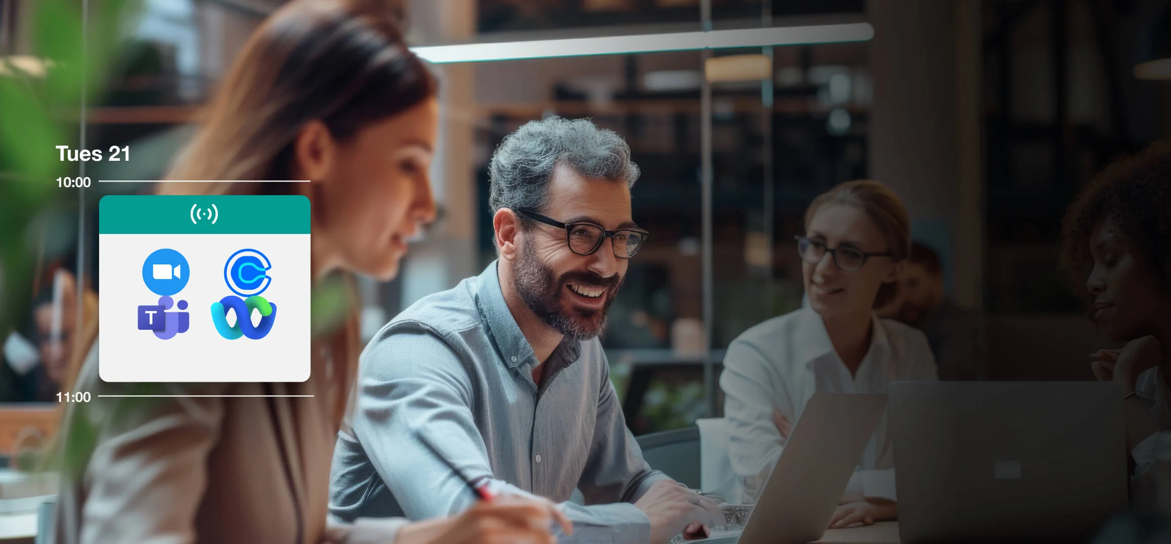 Schedule panel (Tues 21; 10:00 — 11:00) shows four meeting app icons while colleagues chat and work on laptops around a glass-walled conference table.