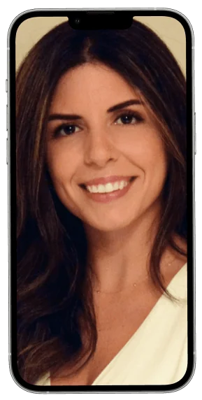A woman with long brown hair smiles close-up, framed by a smartphone screen against a neutral beige background, wearing a white top.