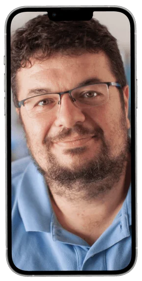 Smartphone screen shows a close-up portrait of a bearded man wearing glasses and a light-blue polo, smiling gently while looking at the camera...