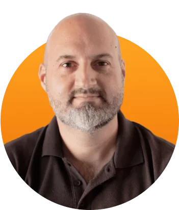 Bald man with trimmed gray beard gazes calmly at the camera, wearing a dark polo shirt against a bright orange circular backdrop.