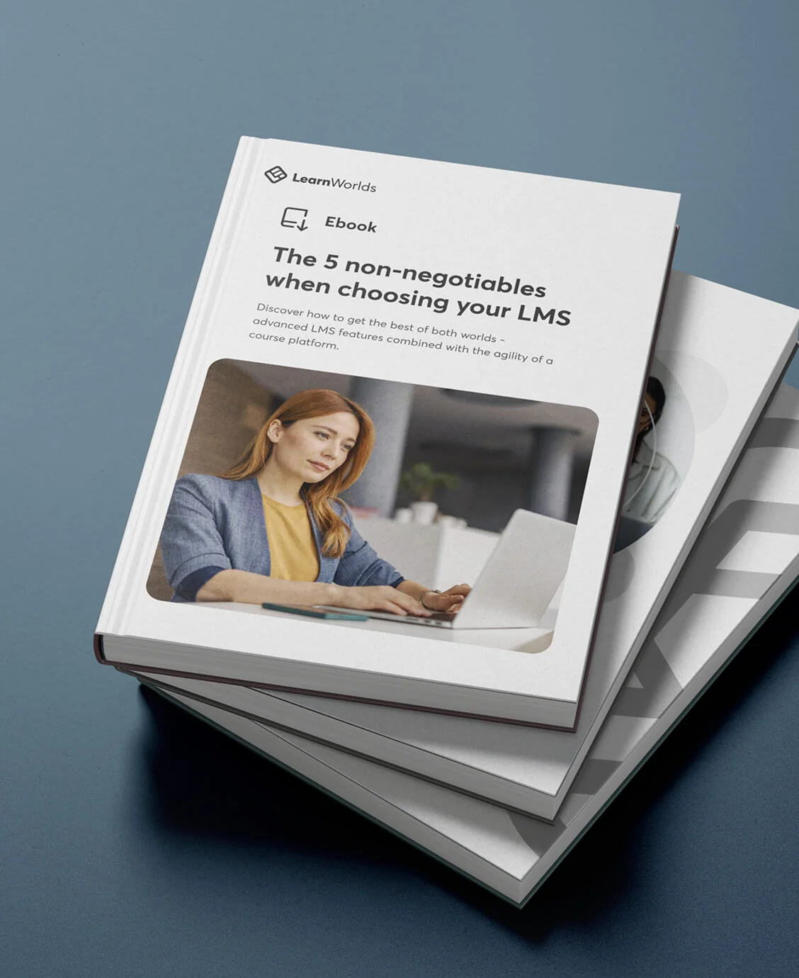 A white e-book resting atop two copies on a blue surface; the cover shows a woman typing at a laptop and a bold headline about selecting an LMS.