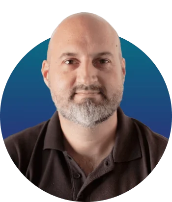 Bearded, bald adult man looks straight ahead with a neutral expression, centered in a circular frame against a blue gradient background, wearing a...