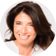 Head-and-shoulders portrait of a smiling woman with shoulder-length dark brown hair and a white top, facing the camera against a plain white...