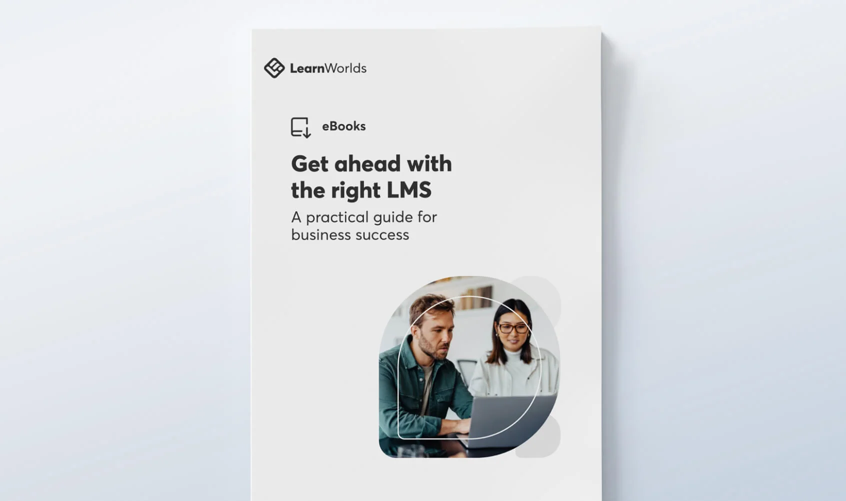 A white ebook cover displays bold title text and a circular photo of two colleagues using a laptop, set in a minimal layout with LearnWorlds branding...